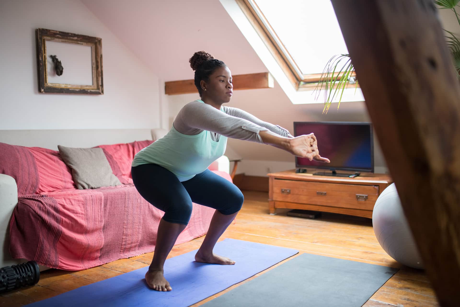 Woman doing a bodyweight squat in a living room with a rug and couch behind her