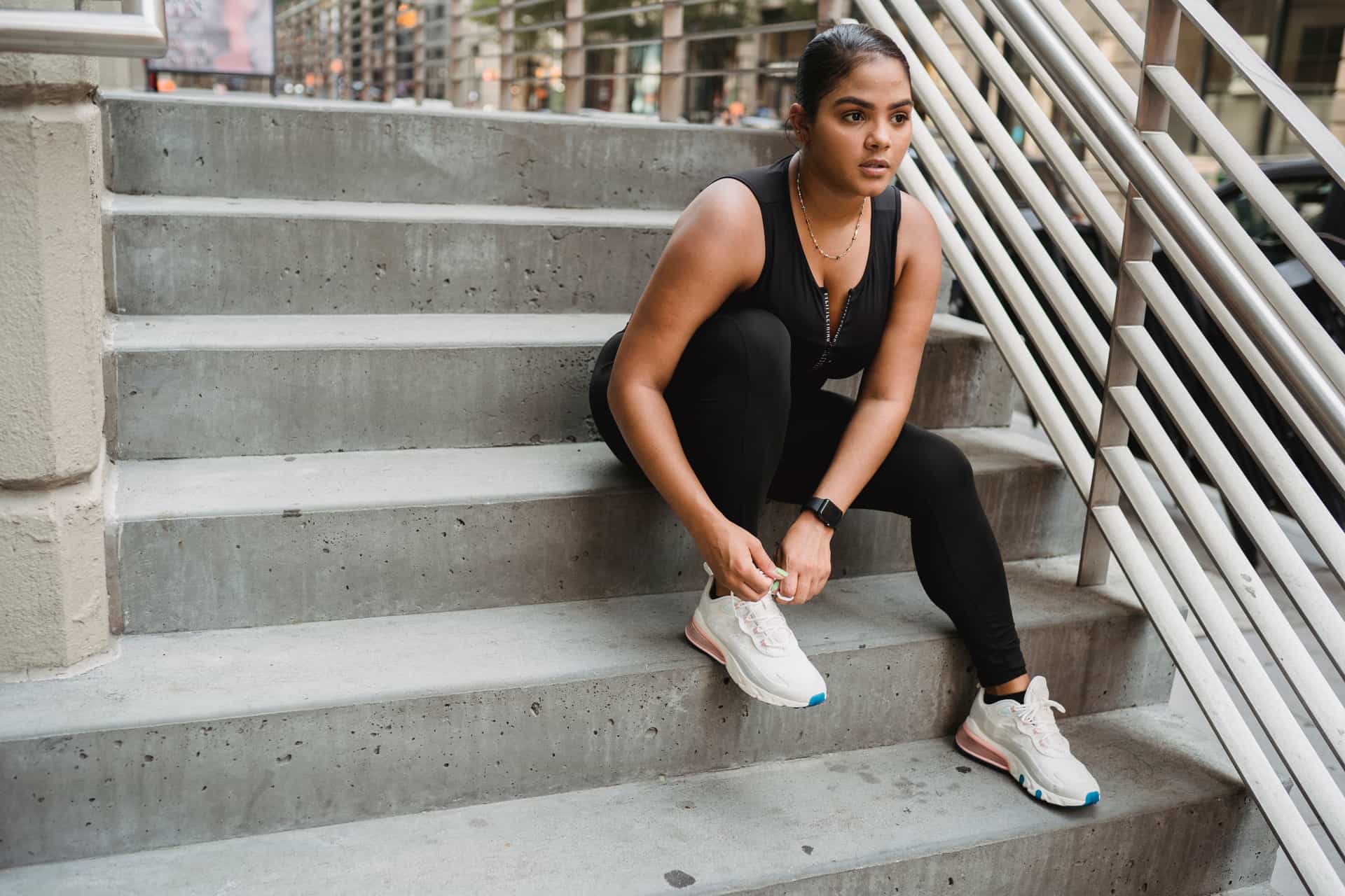 Woman sitting on concrete stairs tying her running shoe before a workout